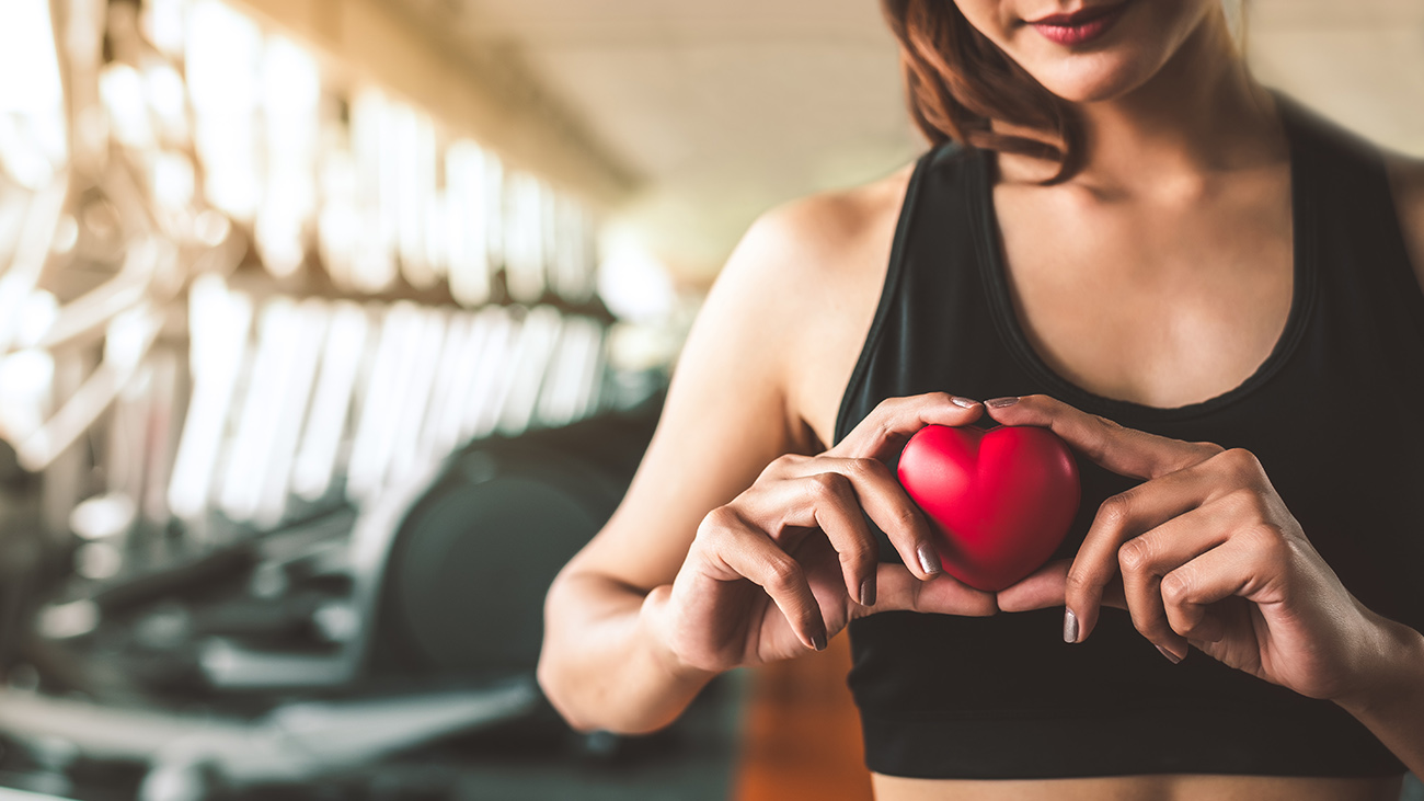 Woman in gym holding a red heart to represent heart health